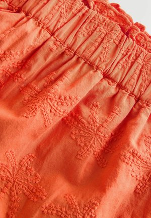 Oranssi kangas, jossa kirjailtuja lehtikuvioita. Yläosassa laskostettua smokkauksena. Pehmeä rakenne, kevyt ja hengittävä materiaali.