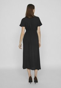 Čierne šaty po kolená s krátkymi rukávmi a elastickým pásom. Hladká textúra. Nosia sa s hnedými lodičkami s leopardím vzorom. Jednoduchý dizajn.