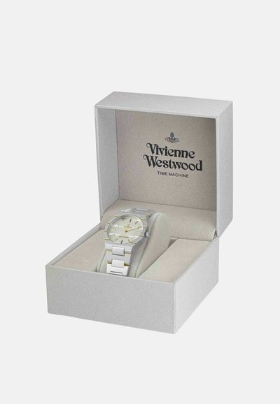 Montre ton argent et or dans une boîte cadeau grise au intérieur doux. La montre présente un cadran rond, un bracelet à maillons et des chiffres arabes.