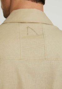 Beiger Leinenhemdkragen mit einem dezenten Stichmuster. Auf der Rückseite in der Nähe des Ausschnitts befindet sich ein auffälliges gesticktes Design.
