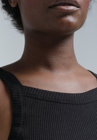 Schwarzes, geripptes Tanktop mit breiten Trägern und einem Rundhalsausschnitt, das einen glatten, strukturierten Stoff auf nackter Haut zeigt.