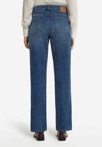 Blå denimjeans med rak bendesign, synliga bakfickor och en tan läderetikett vid midjan.