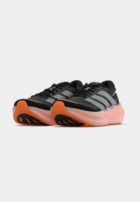 Scarpe da corsa nere con strisce grigie, dotate di tomaia leggera, suola arancione e suola esterna nera testurizzata per una maggiore trazione.