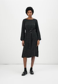 Svart midikjole med blomstermønster, lange ermer, rund hals, innsnevret midje med belte, og en utsvingt skjørt. Brukt med svarte loafers.