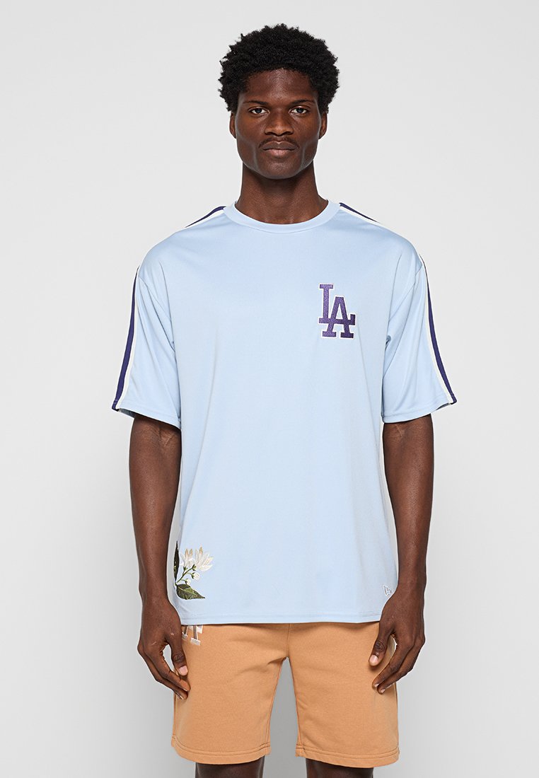 Jasnoniebieska koszulka z krótkim rękawem wykonana z gładkiego materiału, z ciemnoniebieskim paskiem i haftem kwiatowym na dole.