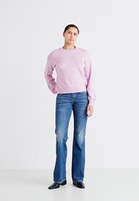 Pulover tricotat lila, cu un model texturat și guler rotund, asortat cu blugi evazați de un albastru estompat și pantofi negri cu vârf ascuțit.