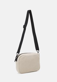 Borsa a tracolla in corduroy beige con tracolla nera regolabile, forma rettangolare, chiusura con zip e texture trapuntata.