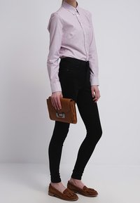 Gestreifte pinke Hemdbluse, schwarze Skinny-Jeans, braune Ledertasche und braune Loafers mit Quasten-Detail. Glattes Material und taillierte Passform.
