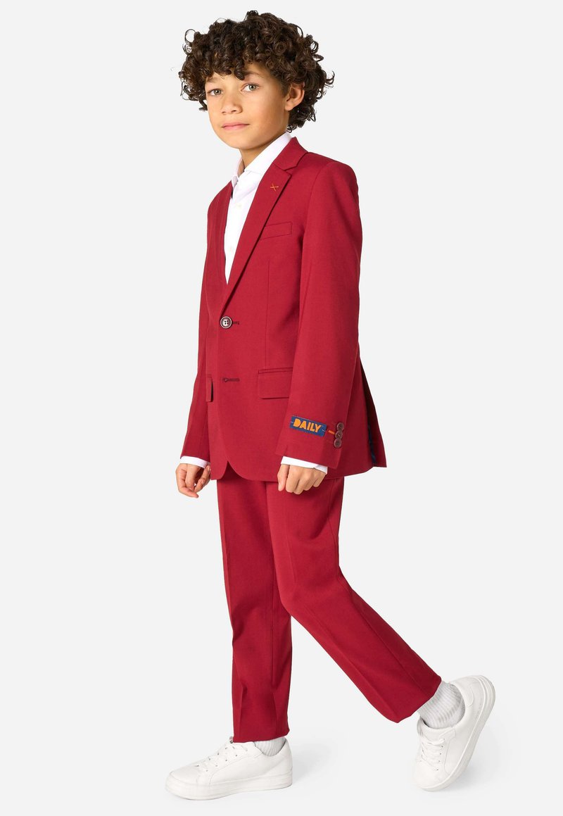 Completo su misura rosso con blazer a un bottone, fazzoletto da taschino e patch "DAILY" sulla manica, abbinato a sneakers bianche.