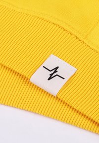 Yellow ribbed fabric with a white label featuring a black logo. The fabric has a smooth texture with visible stitching details.