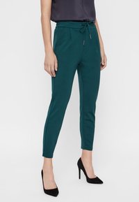 Teal tapered byxor i mjukt material med justerbart dragsnöre i midjan, med sidofickor och en slät textur.