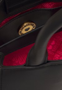 Mustapohjainen laukku, jossa on punainen vuori, jossa on "Love Moschino" -teksti ja kultainen napin sulkeminen, johon on painettu "Love Moschino" ja sydämen muotoisia kuvioita.