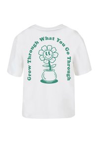 Hvid bomulds t-shirt med en grøn grafik af en smilende blomst i en potte og teksten "Vokse gennem det, du går igennem" omkring den.