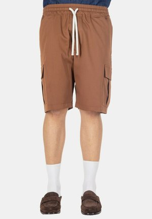 Pantaloncini cargo marroni fino al ginocchio con coulisse bianca, indossati con calzini bianchi e scarpe slip-on marrone scuro.