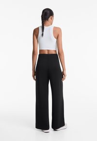 Top court en coton blanc côtelé associé à un pantalon large noir taille haute, tissu lisse, coutures minimales et petites fentes sur les côtés au niveau de l'ourlet.