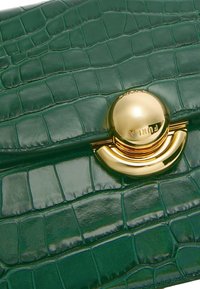 Grüne Handtasche aus Kunstleder mit Krokodilprägung und glänzender Oberfläche, ausgestattet mit einem goldenen, runden Verschluss und einer strukturierten Oberfläche mit gitterartigen Mustern.