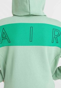 Ljusgrön hoodie med ett mörkgrönt horisontellt band som har ordet "AIR" i feta svarta bokstäver över ryggen. Mjuk textur, avslappnad design.
