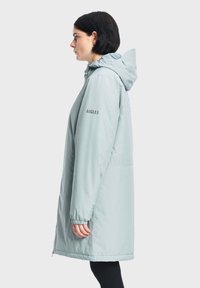 Parka azzurro chiaro, lungo fino al ginocchio, con cappuccio, polsini elasticizzati, tasche laterali e il nome del marchio "AIGLE" sulla manica. Tessuto liscio e strutturato.