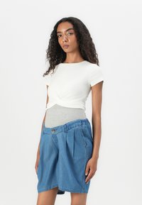 Hvit t-skjorte med kort erm og vridd front, lagd over en grå tettsittende underdress, kombinert med blå denimshorts med knapp og legg.