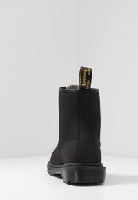 Zwarte enkellaarsjes met een gestructureerd bovenwerk, een stevige zool en een opvallende gele lus met het label "WITH Bouncing SOLES".