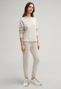 Beige Baumwoll-Sweatshirt mit langen Ärmeln und Rundhalsausschnitt, kombiniert mit passenden schmalen Hosen und weißen Sneakers mit goldenen Akzenten.