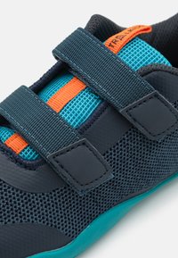Jūras spēku acu apavi ar tirkīza akcentiem, ar oranžām siksnām un teksturētu audumu. Dizainu noslēdz Velcro aizdare un gumijas zole.