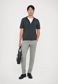 Polo majica tamnosive boje kratkih rukava sa razdvojenim ovratnikom, uparena sa svijetlosivim hlačama. Model drži crnu torbu preko ramena i nosi crne cipele.