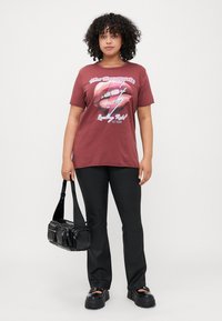 Maroon graphic t-shirt with a lips and lightning bolt design, paired with black flared pants and a black patent handbag. Chunky black shoes.