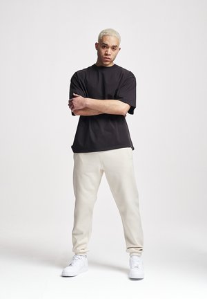 Dunkles kurzärmliges T-Shirt, kombiniert mit hellbeigen Jogginghosen und weißen Sneakern, das eine entspannte Passform und eine glatte Stoffstruktur zeigt.