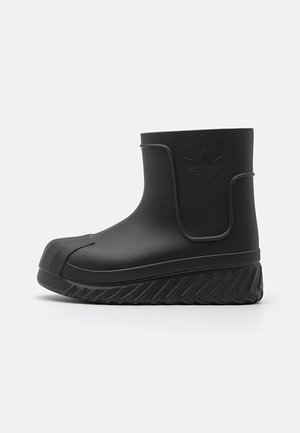Stivale alla caviglia impermeabile nero con suola in gomma texture, tomaia liscia, logo in rilievo e design a punta tonda. Caratterizzato da uno stile slip-on con una costruzione robusta.