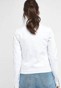 White denim jacket with a fitted design, visible seams, buttoned cuffs, and a slightly cropped length, paired with light blue jeans.
