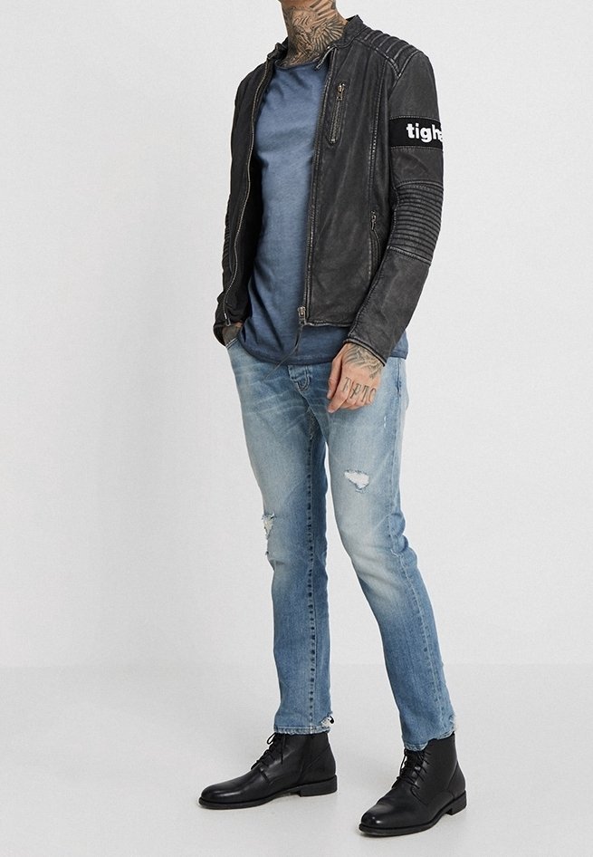 Sort læder bikerjakke med ribbet tekstur, blå t-shirt, lyse slidte jeans og sorte snørestøvler.