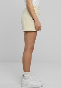Beige träningsshorts med elastisk midja, sidfickor och slät textur, i kombination med vita sneakers och ankelsockor.