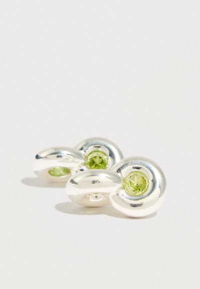 Hopeiset korvakorut, joissa on sileä, kaareva muotoilu, keskellä kaksi vihreää jalokiveä, jotka heijastavat valoa kiillotetulla pinnalla.