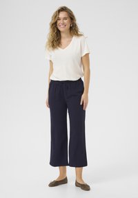 T-shirt beige chiaro a V abbinato a culottes blu scuro larghi, con vita elastica, completato da ballerine marroni.