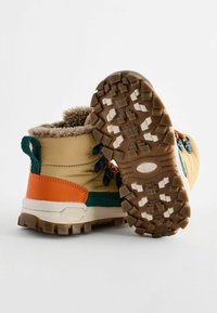 Tan Wanderschuhe mit orangen, blauen und grünen Akzenten, ausgestattet mit einer strukturierten Sohle und einem flauschigen Kragen für zusätzlichen Komfort und Halt.