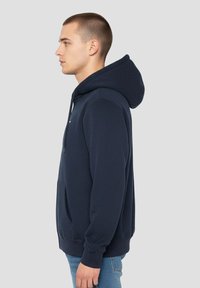Marineblauwe hoodie van zachte stof, voorzien van een kangoeroezak, verstelbare capuchon met trekkoord, en geribbelde boorden en zoom.