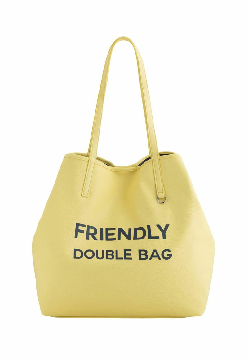 Bolso tote amarillo con una superficie texturizada, que presenta "BOLSA DOBLE AMIGABLE" en letras negras en negrita. Incluye asas largas y delgadas para llevar.