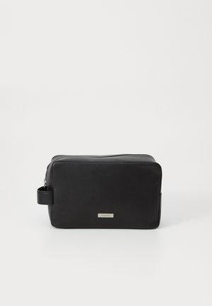 Black leather toiletry bag with rectangular shape, zip closure, side handle, and silver logo plate on the front. Smooth texture.