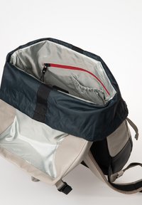 Zaino con un esterno in nylon grigio, un lembo in tessuto blu navy, una fodera argento lucido e una tasca interna con zip rossa. Spallacci regolabili attaccati.