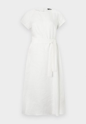 Žena oblečená v biele midi šaty s krátkymi rukávmi a zviazaným opaskom v páse, v kombinácii s čiernymi plochými topánkami, stojaca na bielom pozadí.