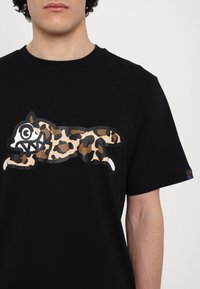 Black cotton t-shirt featuring a large, playful leopard-print graphic of a cartoon animal with an exaggerated face, displayed centrally.
