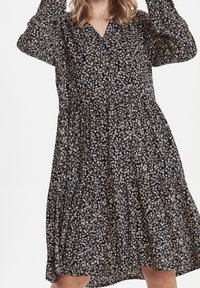 Blommönstrad klänning i svart, med långa ärmar, V-urringning och en lager-på-lager, lös passform. Tyget verkar lätt och mjukt.