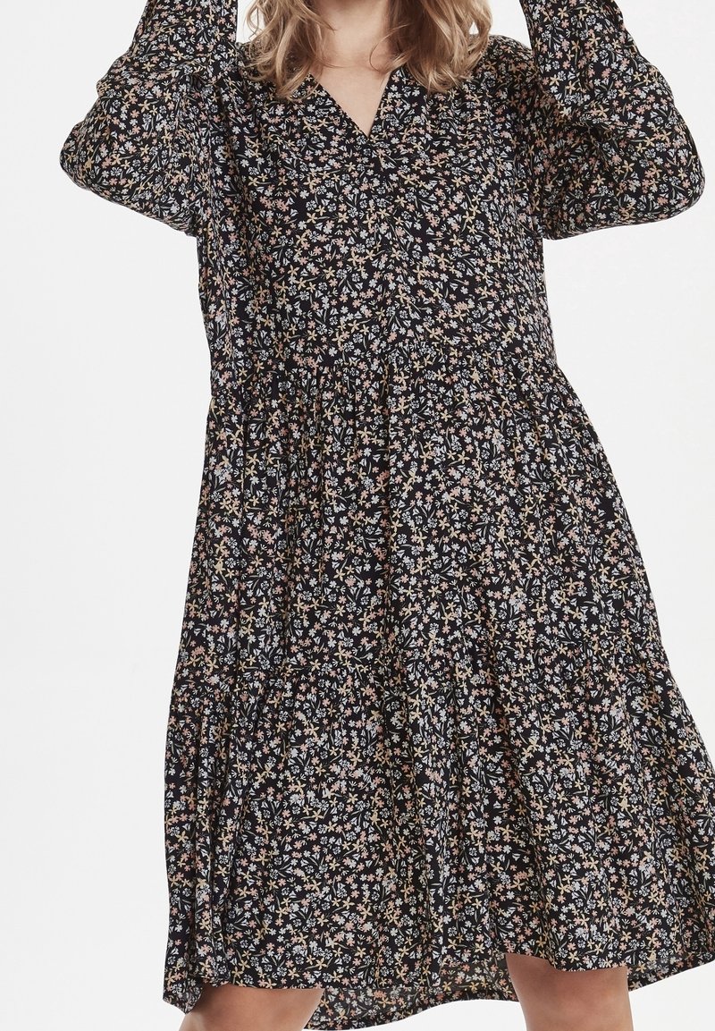 Blommönstrad klänning i svart, med långa ärmar, V-urringning och en lager-på-lager, lös passform. Tyget verkar lätt och mjukt.