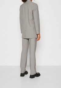 Traje a rayas grises con un blazer largo y pantalones a juego. El material parece suave con un ajuste estructurado. Zapatos negros complementan el atuendo.