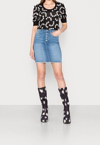 Top negro de manga corta con patrón floral blanco, combinado con una falda de mezclilla azul claro y botas altas oscuras hasta la rodilla que presentan margaritas blancas.