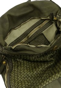 Olive green leather bag interior with multiple zippered pockets, woven texture, and contrasting lighter material. Features visible brand tag.