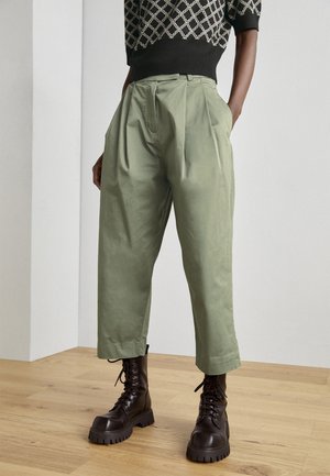 Lichtgroene, geplooide broeken van katoen met een relaxed fit. G gedragen met zwarte veterschoenen met een grove zool.