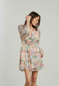 Blumenmusterkleid mit V-Ausschnitt, langen Ärmeln und Rüschendetails. Leichtes, pastellfarbenes Material mit gestuften Lagen.