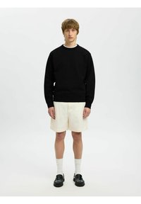 Sudadera negra, pantalones cortos crema, calcetines blancos y mocasines negros. Diseño sencillo, puños y dobladillo ajustados, con un escote redondo en la sudadera.